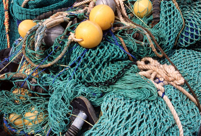 Tangled green fishing nets with yellow floats and ropes piled on deck, ready for commercial fisheries use.
